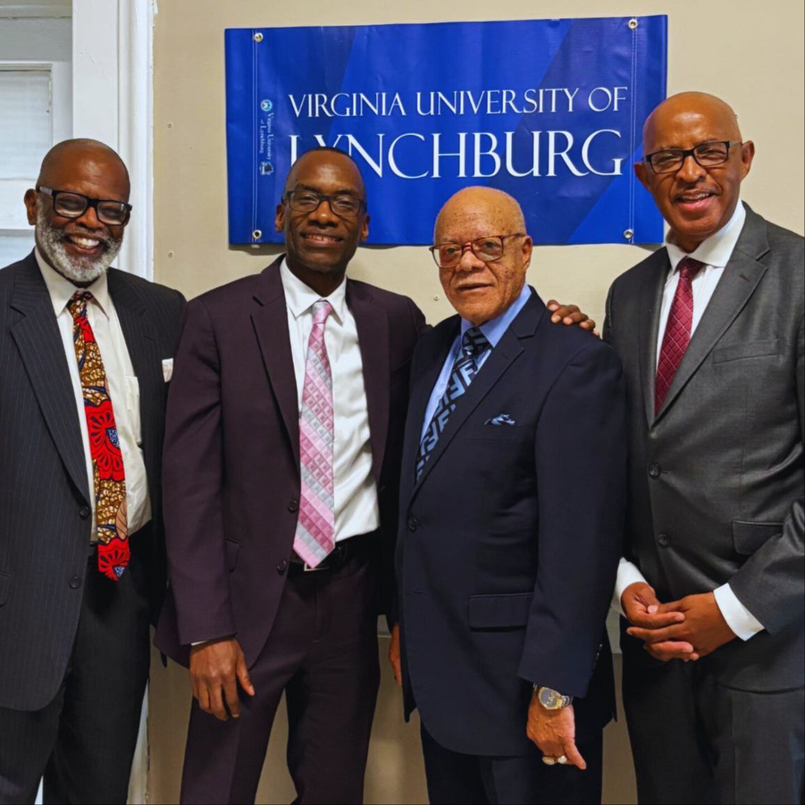 Three people standing together in front of the Virginia University of Lynchburg logo.